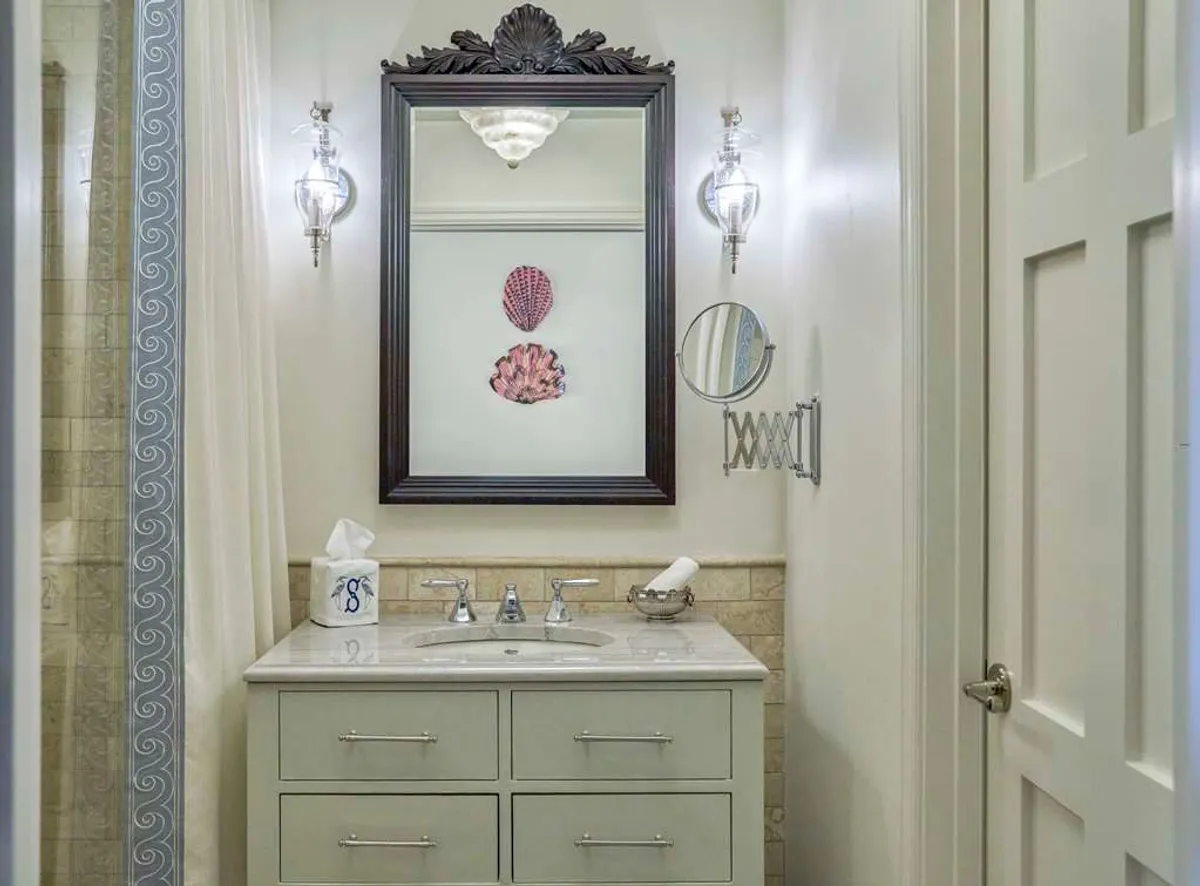 A calm bathroom interior featuring an ornate framed mirror above a vanity with a sink, complemented by colorful shell art. The setup suggests a space ideal for grooming, relaxation, and self-care, with an atmosphere that evokes spa-like rejuvenation.