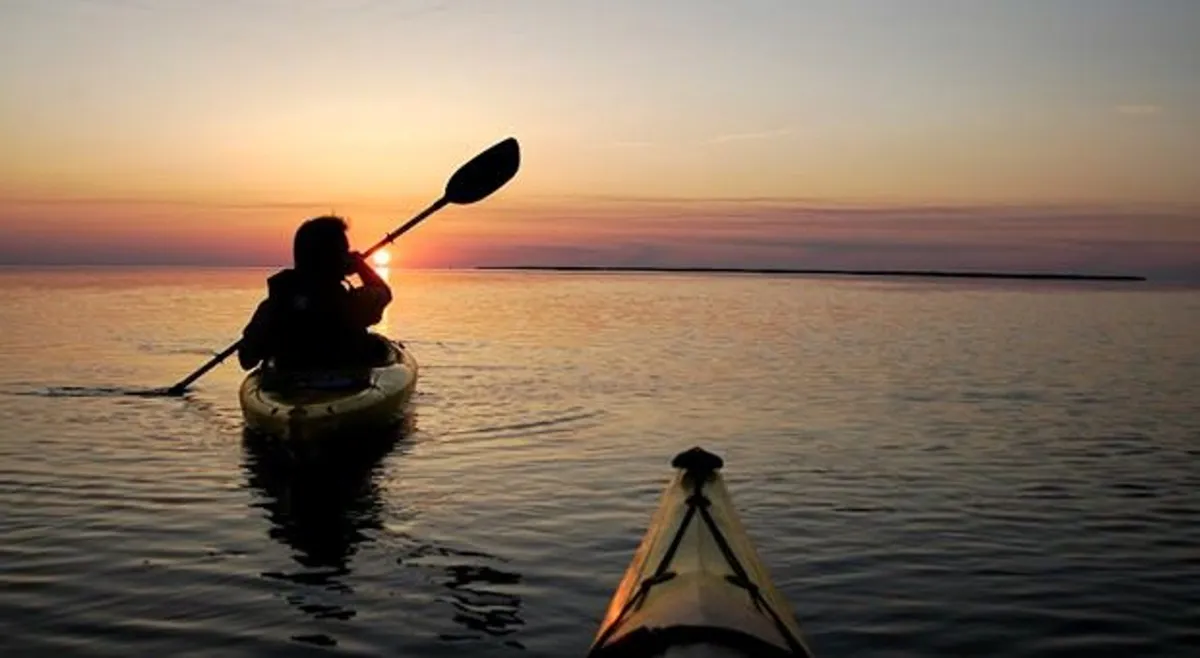 A tranquil view of a person kayaking on calm water at sunset, with rich colors reflecting off the surface. The image captures both the serenity and the spirit of exploration that the resort offers through guided tours and nature-focused excursions.