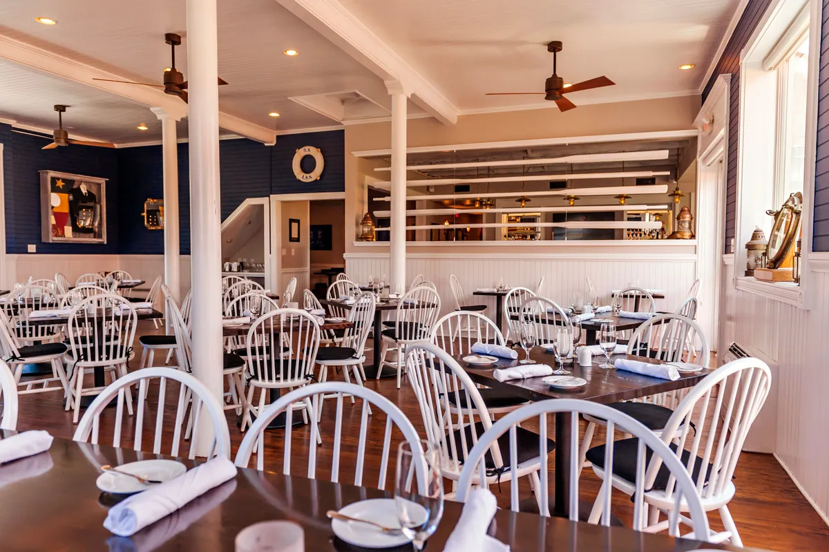 A cheerful restaurant-style setting with wooden tables, white chairs, a visible bar area, and decorative wall art. The scene is set for socializing, dining, and celebrating, with a relaxed vibe that invites guests of all abilities to enjoy shared experiences.