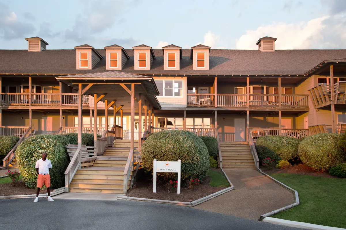 This image captures the property’s entrance stairs and porch at sunset, with the beach house sign visible and a figure standing in front. The mood is warm and inviting, hinting at relaxed evenings and the promise of winding down together as day fades into night.